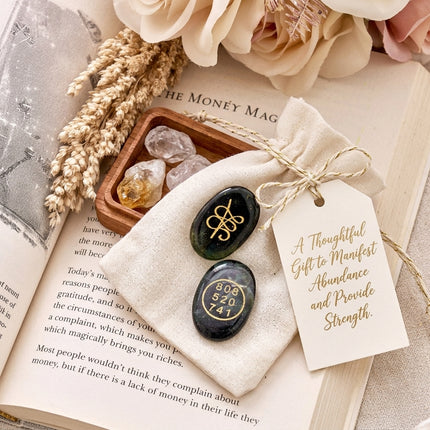 Zibu and Grabovoi wealth coins placed on a gift bag with a tag that reads "A Thoughtful Gift to Manifest Abundance," set against a book about money manifestation