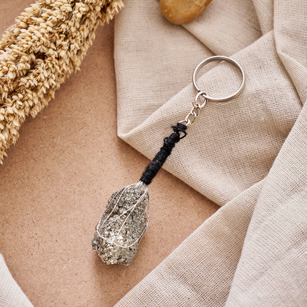 A high-quality top-down shot of a natural raw Peruvian Pyrite keychain, showcasing the intricate wire-wrapping and the golden, metallic luster of the abundance stone against a rustic background
